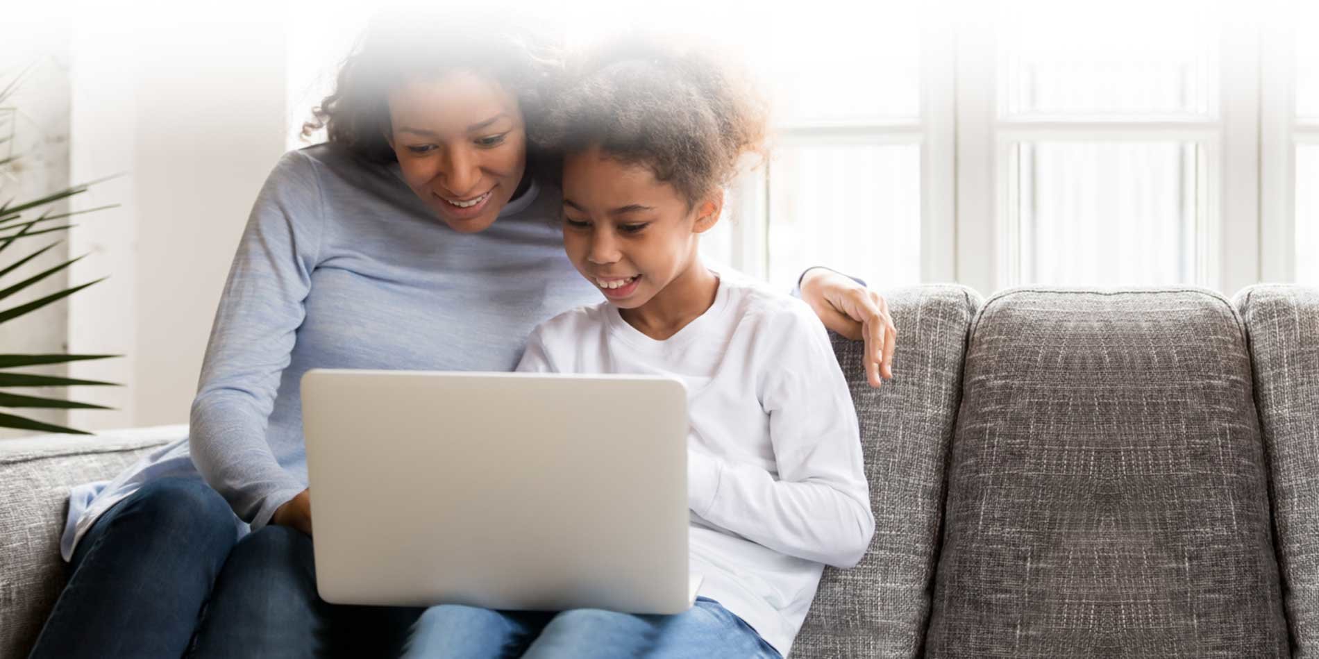 Mom and Daughter on a gray couch looking at a laptop.