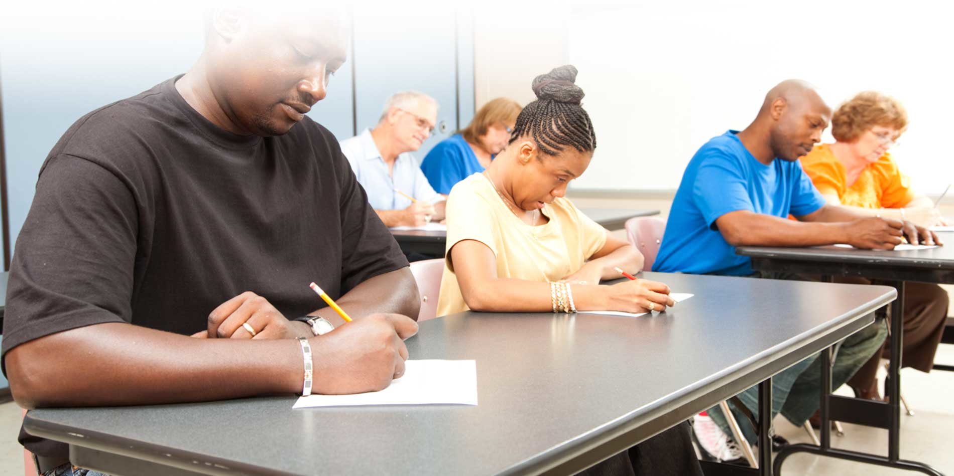 A group of people sitting at individual desks writing on paper.