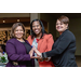 Three women smiling and connecting their hands in a way to display a triangle