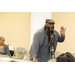 man in gray with hat standing at table talking