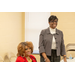 2 women at table talking, 1 standing, 1 sitting